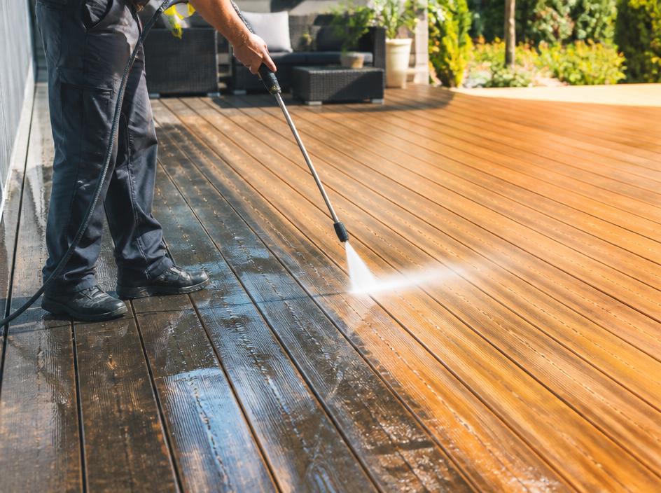 Backyard wooden deck being washed clean with visible bright cleaned boards next to weathered ones